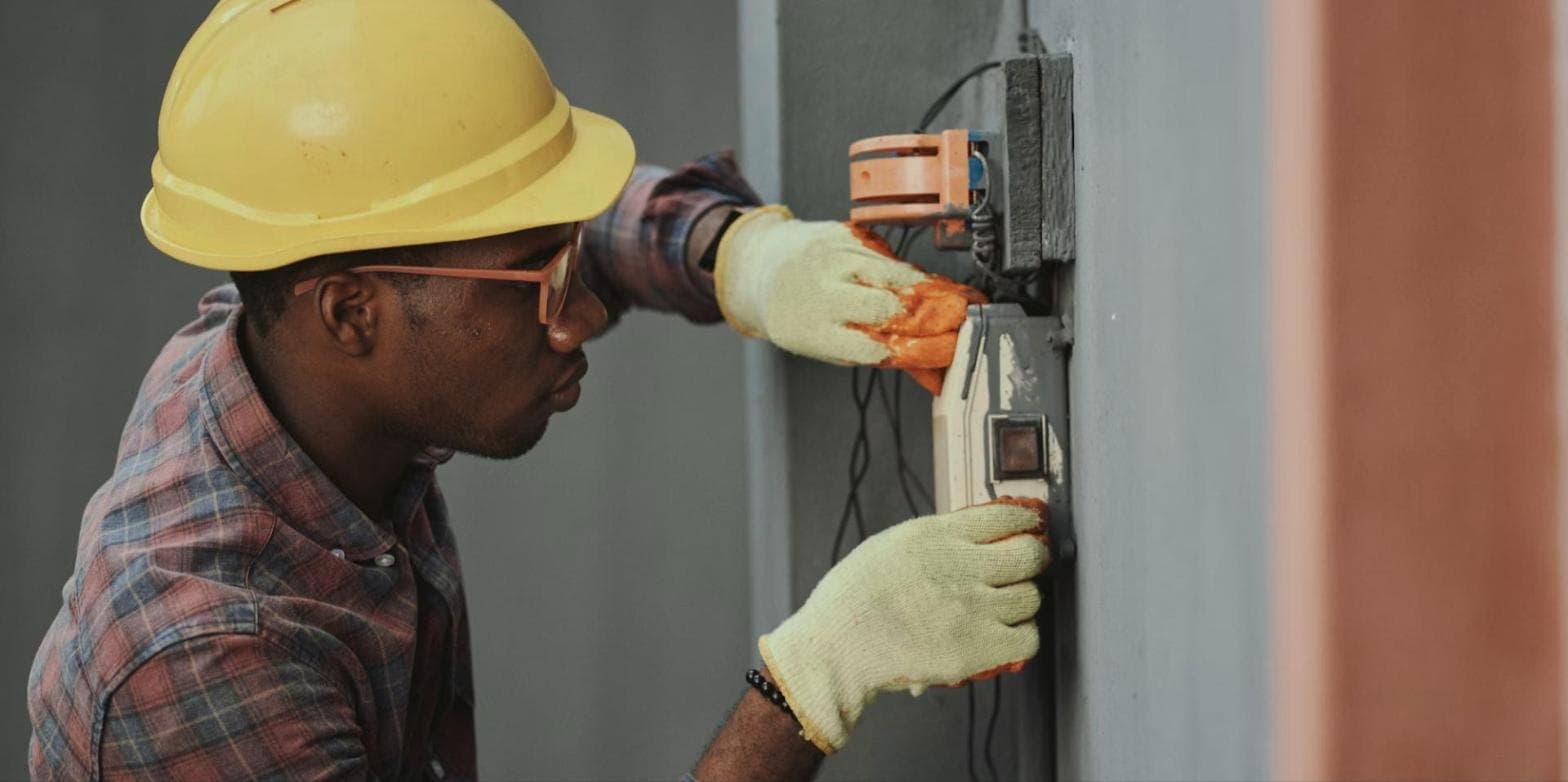 A technician in a hard hat working on an electricity meter